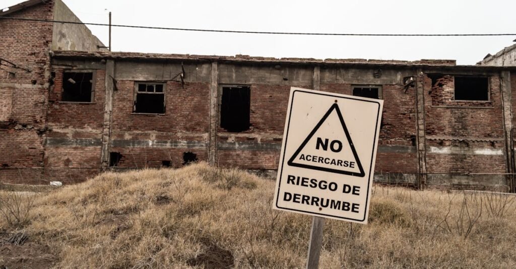 An abandoned brick building with a warning sign indicating risk of collapse in Spanish.