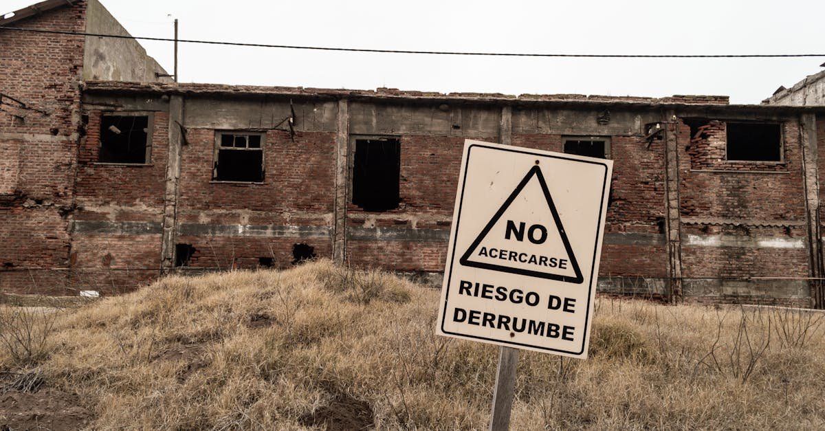 An abandoned brick building with a warning sign indicating risk of collapse in Spanish.